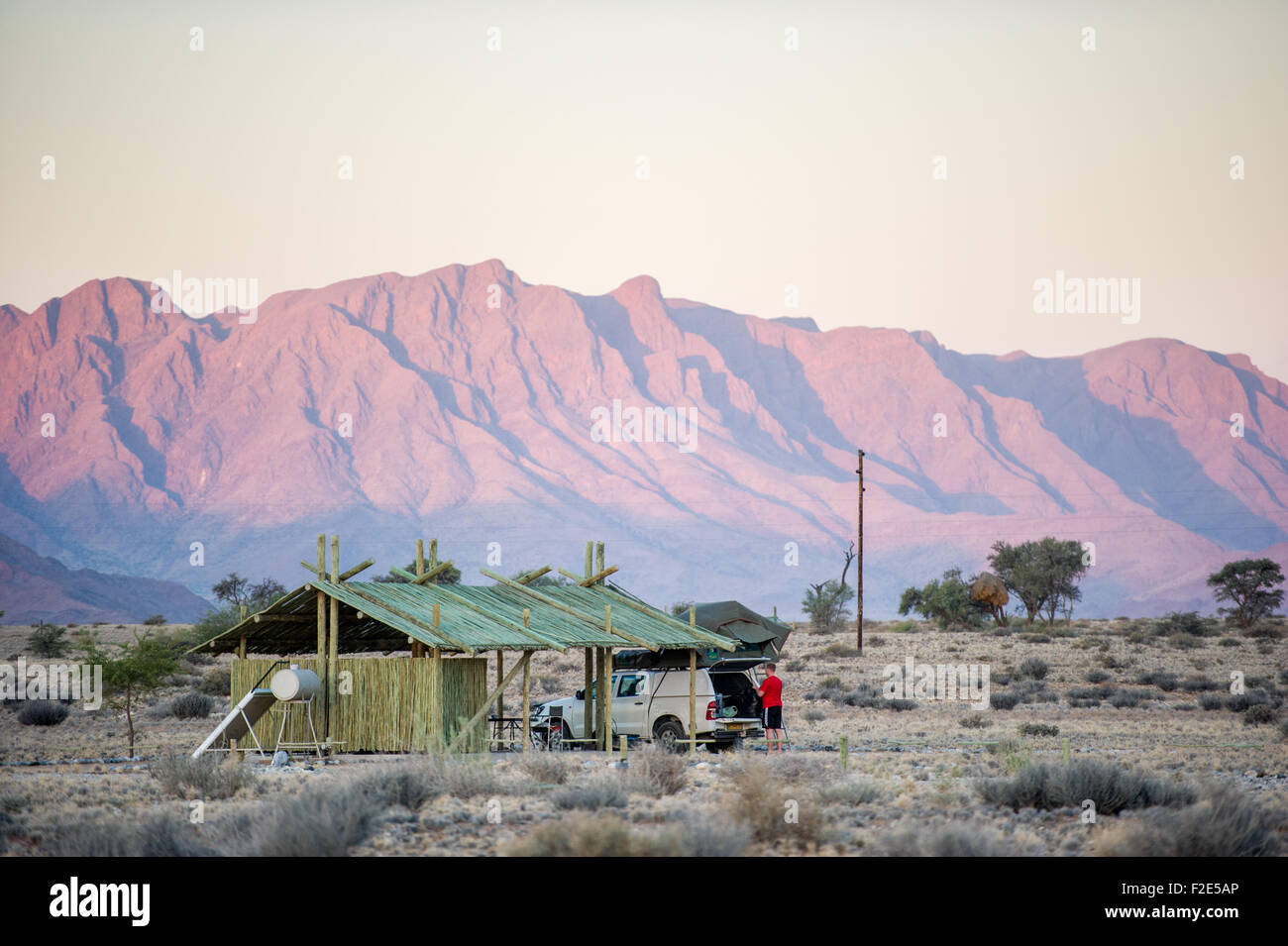 Offene Landschaft mit Berge hinter einem kleinen Haus und Mann Auspacken sein Auto in Sossusvlei Namibia, Afrika Stockfoto