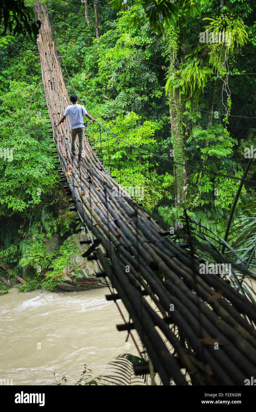 Mann geht auf Bambusbrücke über einen Fluss. Stockfoto