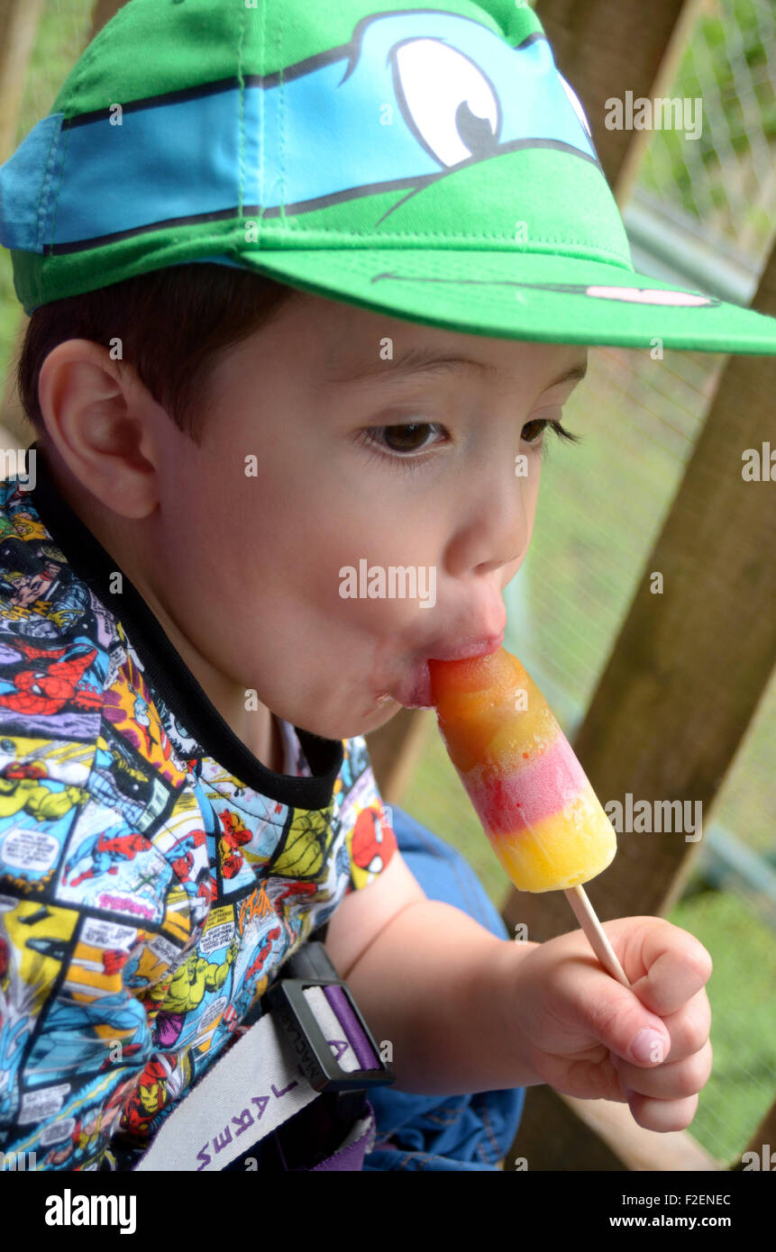 Ein kleiner Junge in eine grüne Baseballmütze isst ein Eis am Stiel. Stockfoto