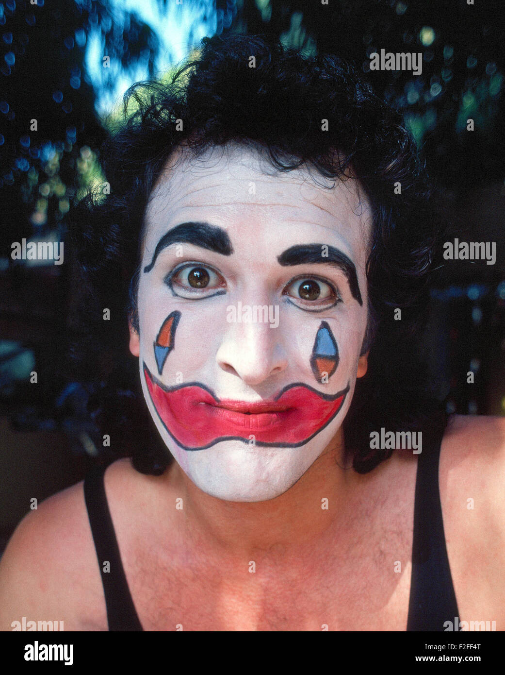Ein männlicher Mime mit einem Lächeln der große rote Lippen gemalt auf seinem Clown Gesicht starrt mit großen braunen Augen in die Kamera für eine informelle Porträt während einer Straße Messe in Kalifornien, USA. Stockfoto