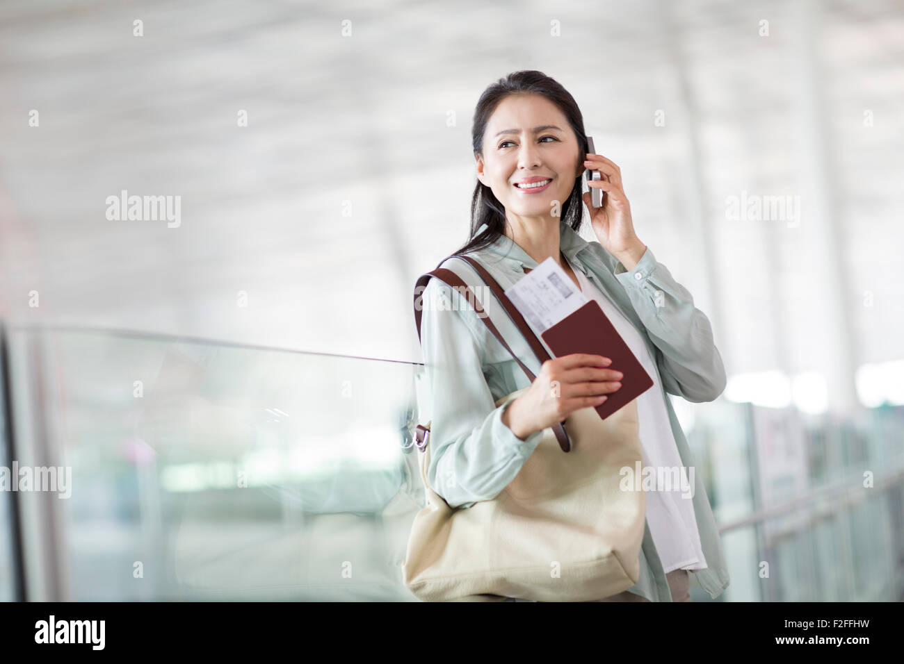 Reife Frau am Telefon am Flughafen Stockfoto