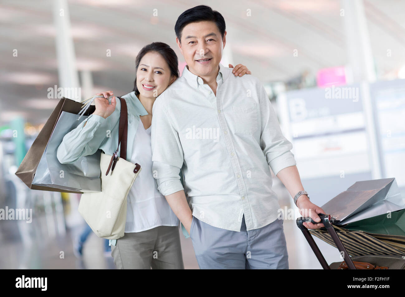 Älteres Paar warten am Flughafen mit Einkaufstüten Stockfoto