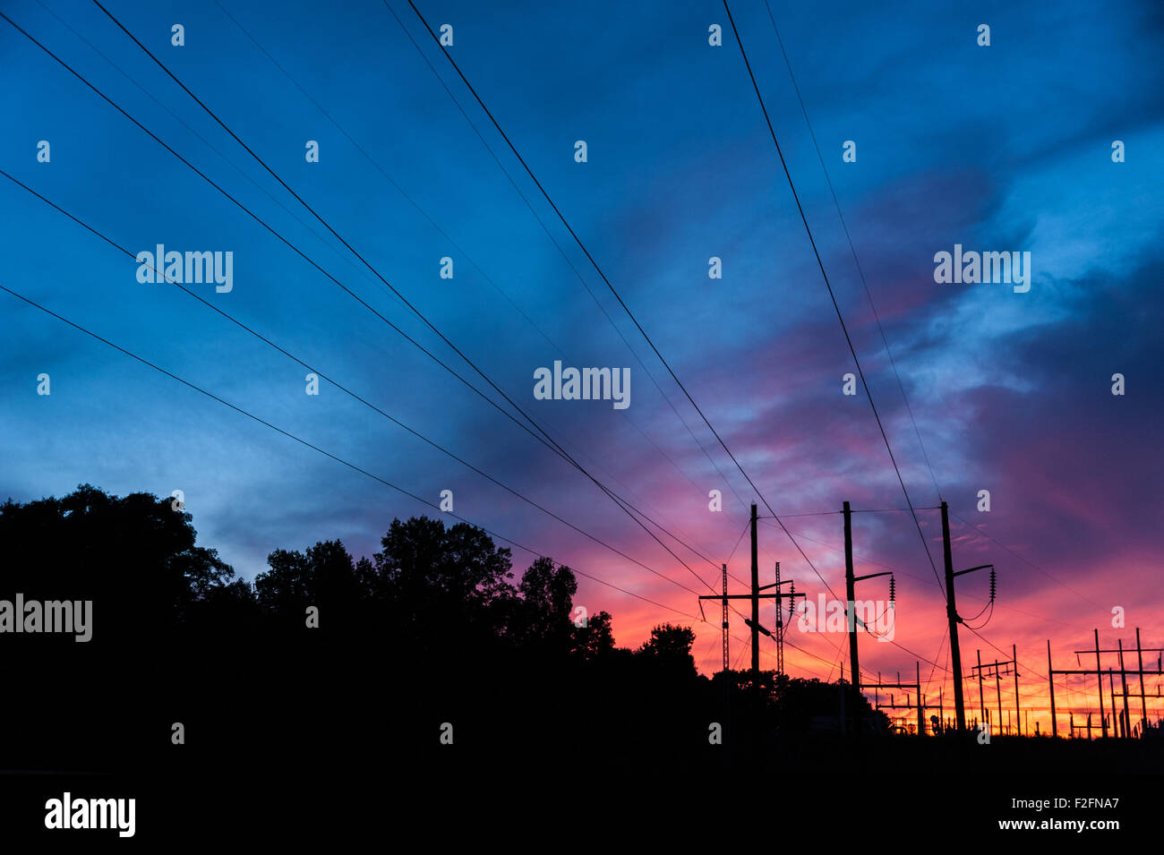 Stromleitungen konvergieren in einem Umspannwerk Silhouette gegen eine lebendige Sonnenuntergang Himmel. Stockfoto