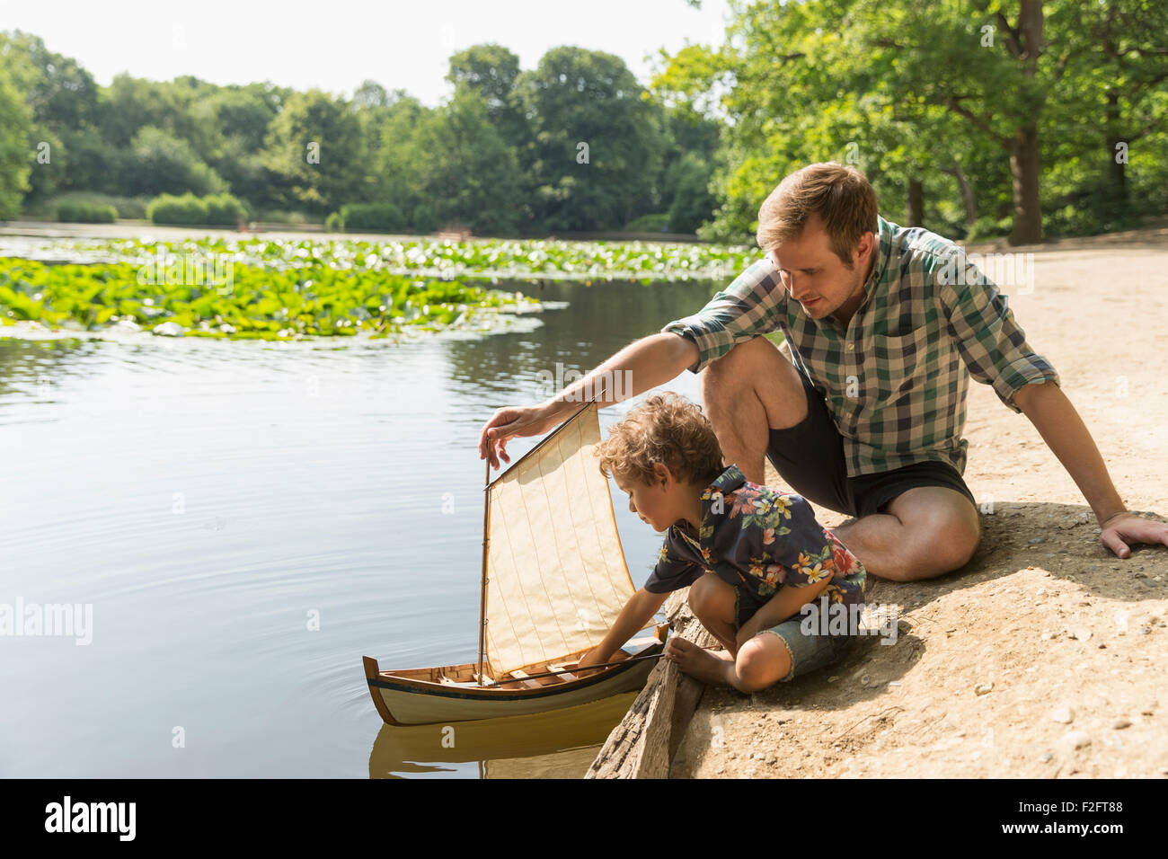 Vater und Sohn spielen mit Spielzeug Segelboot am See Stockfoto
