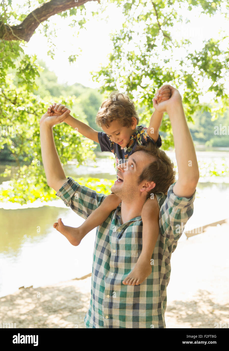 Verspielte Vater mit Sohn auf Schultern am Seeufer Stockfoto