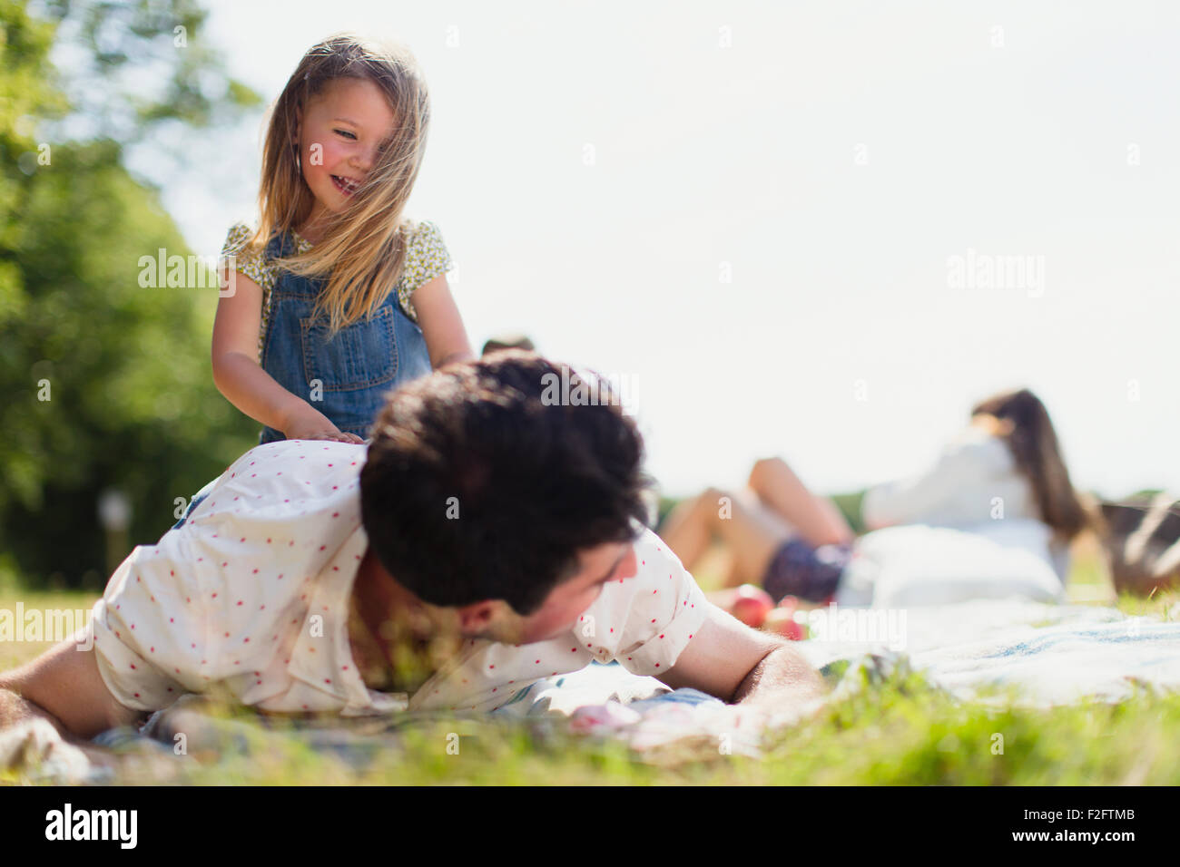 Verspielte Tochter auf Vater im sonnigen Feld Stockfoto