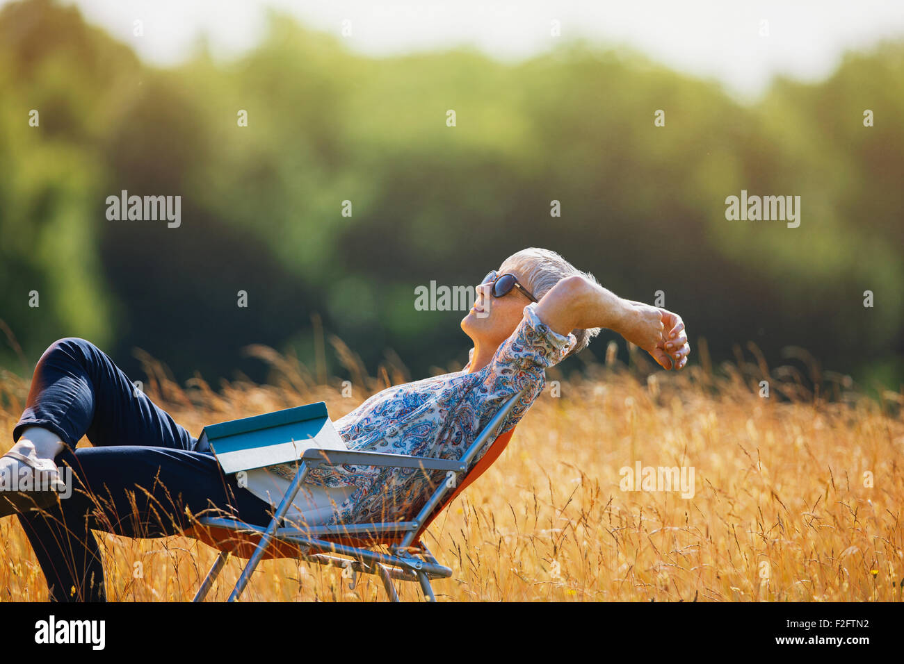 Unbeschwerte senior Frau mit Buch im sonnigen Bereich entspannen Stockfoto