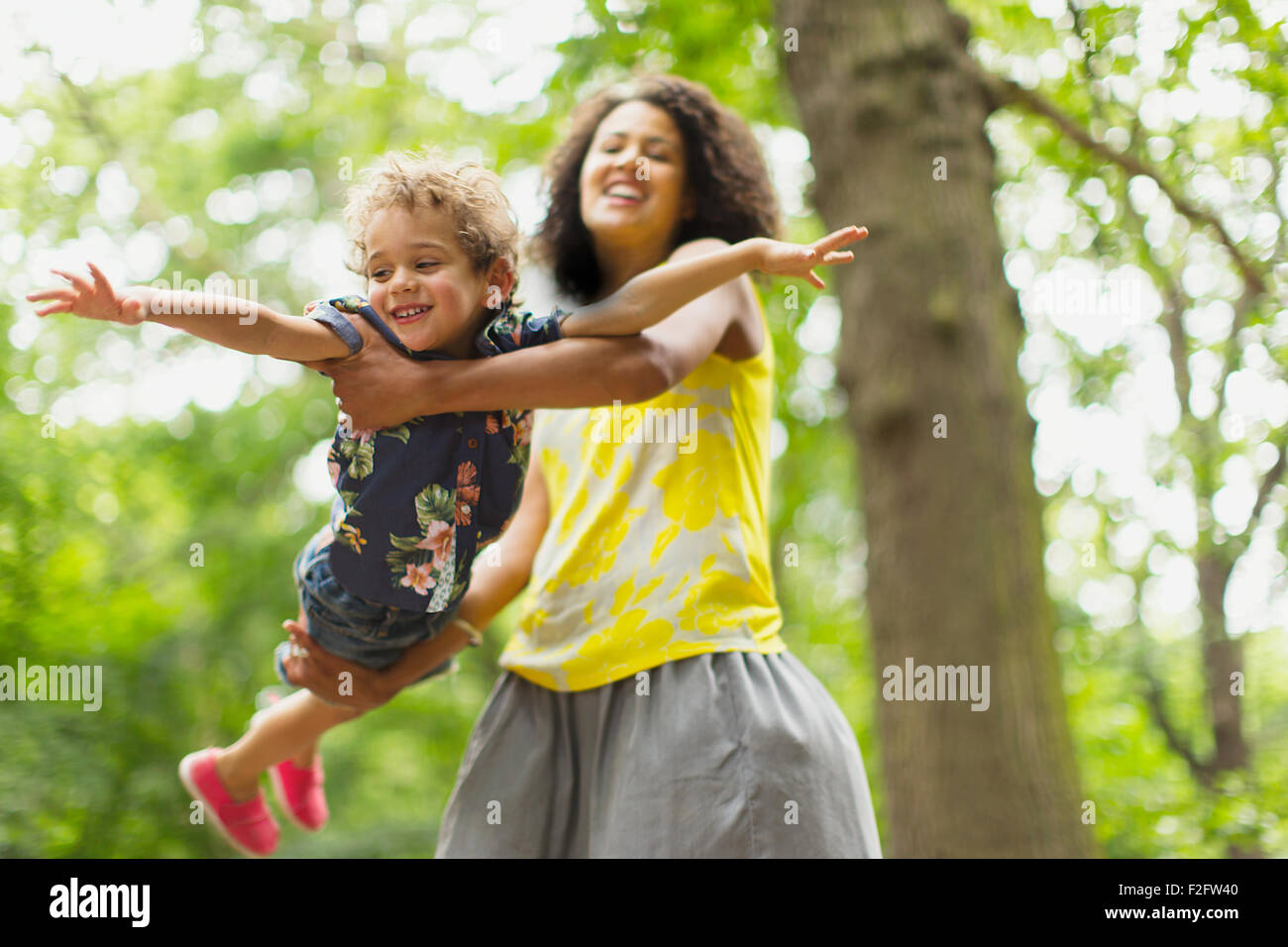 Spielerische Mutter fliegenden Sohn unter Baum Stockfoto