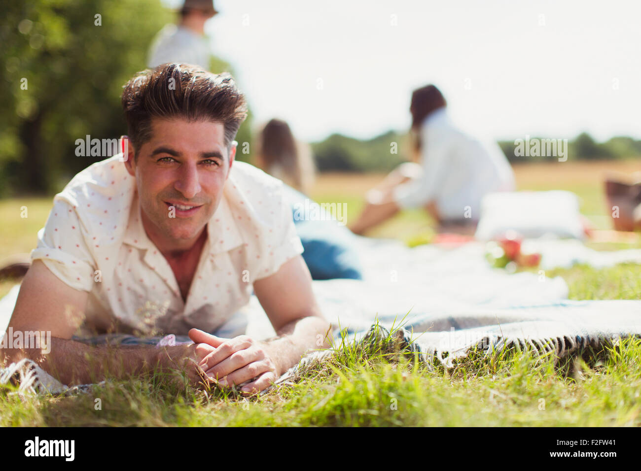 Lächelnder Mann Porträt Handauflegen Picknickdecke im sonnigen Feld Stockfoto
