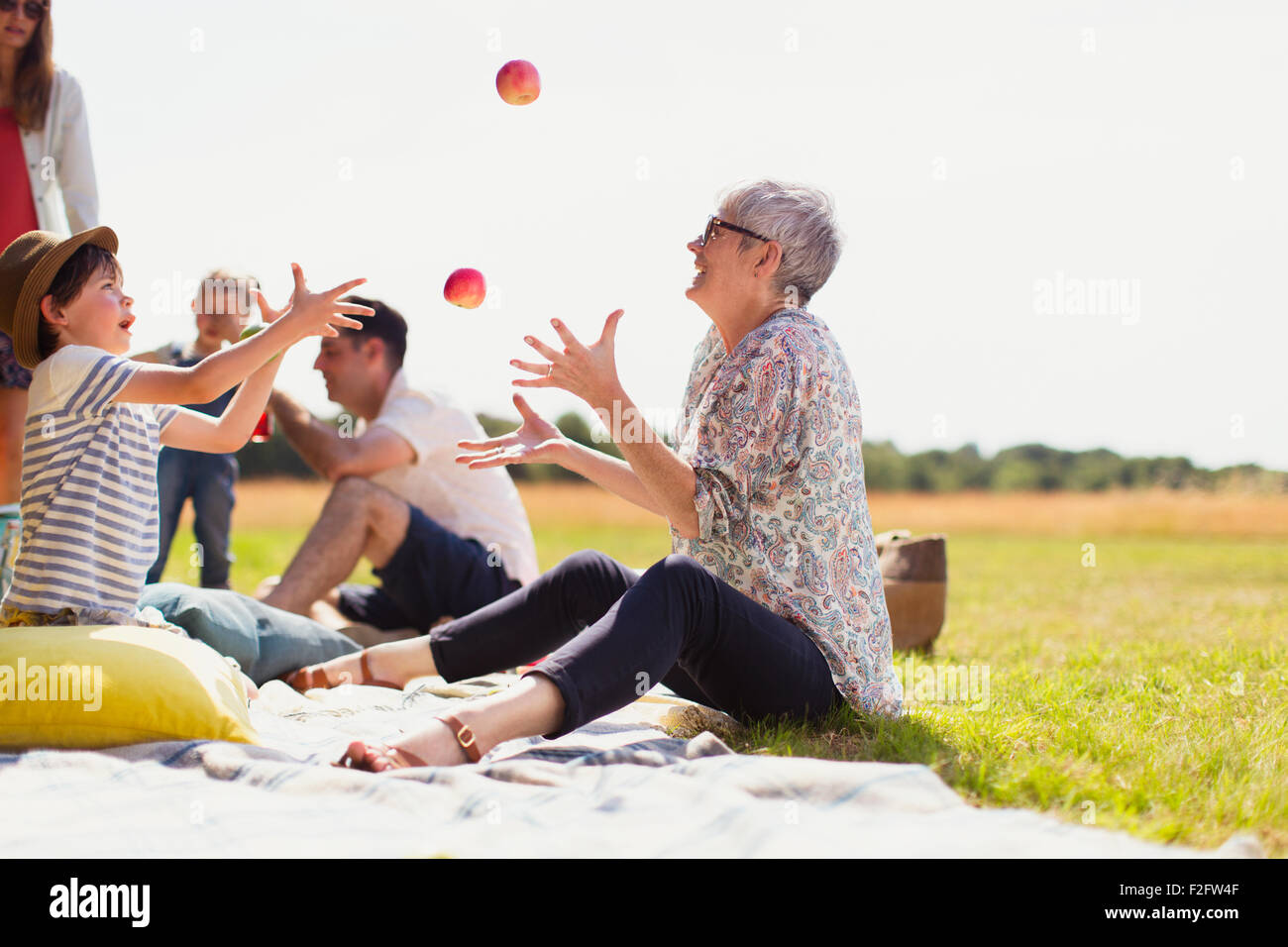 Großmutter und Enkel jonglieren Äpfel auf der Picknickdecke im sonnigen Bereich Stockfoto