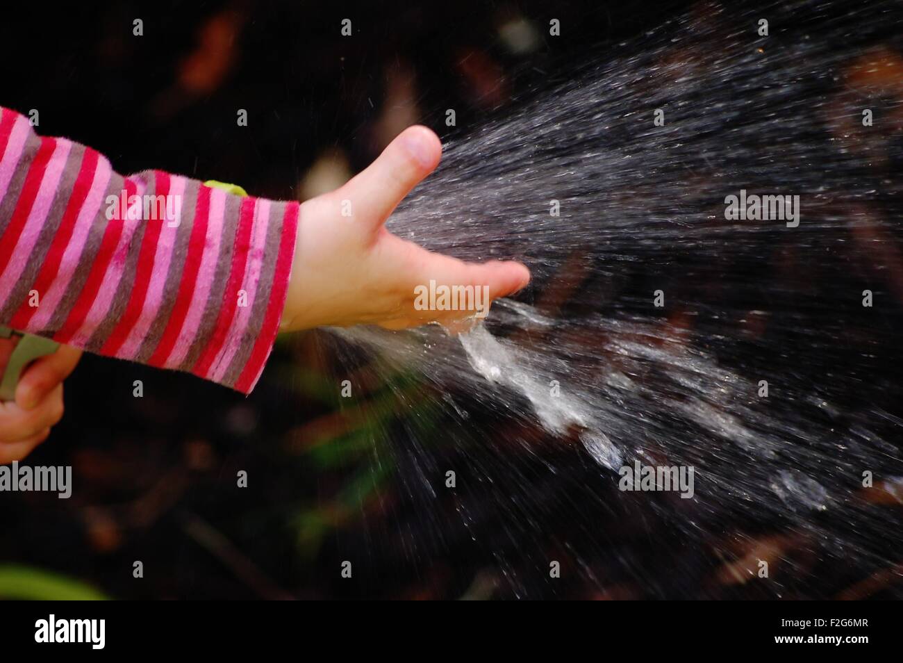 Eine Nahaufnahme von einem kleinen Mädchen spielen mit Wasser aus einem Schlauch Stockfoto