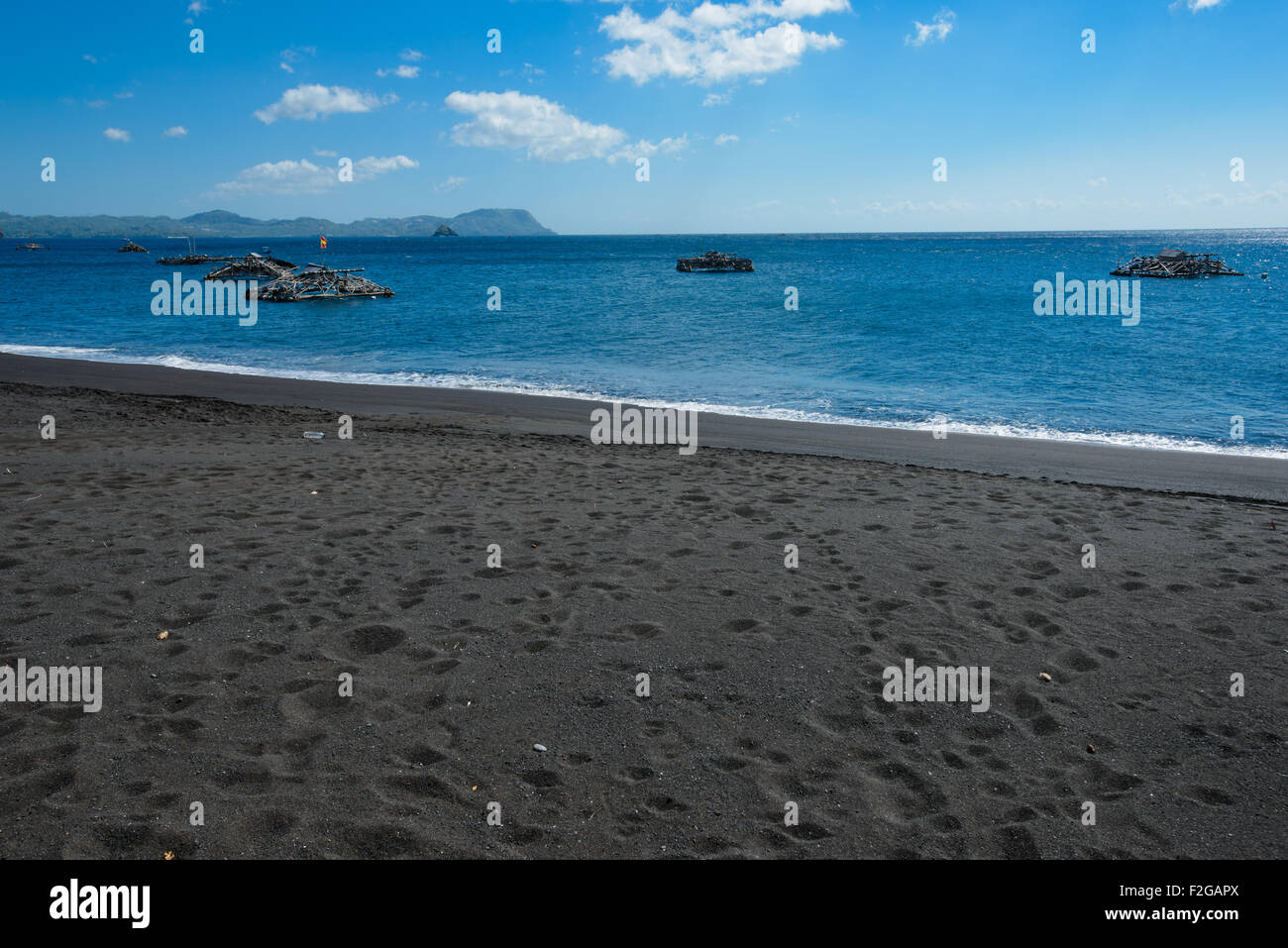 Küste Fischer Hütten in Nord-Sulawesi auf einem schwarzen Sandstrand mit tropischen üppigen im Hintergrund an einem sonnigen Tag mit blau Stockfoto