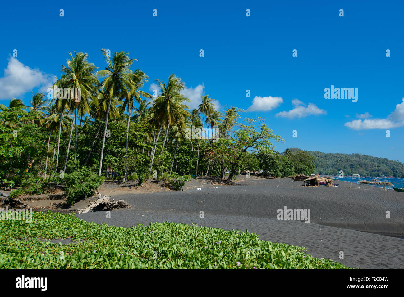 Küste Fischer Hütten in Nord-Sulawesi auf einem schwarzen Sandstrand mit tropischen üppigen im Hintergrund an einem sonnigen Tag mit blau Stockfoto