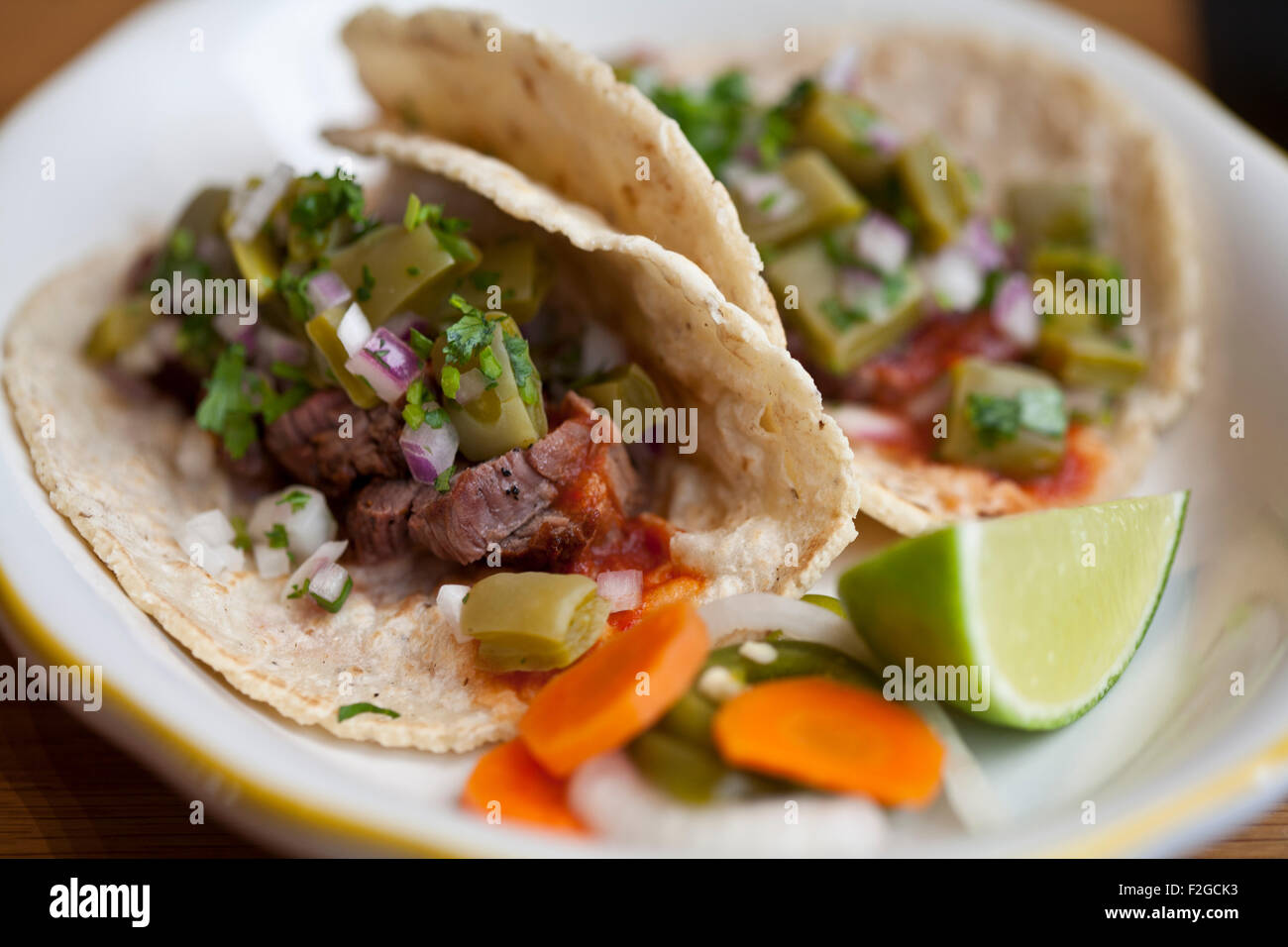 zwei Carne Asada Tacos mit Nopales, Chipotle und Salsa auf einem weißen Teller mit Kalk und eingelegtes Gemüse Stockfoto