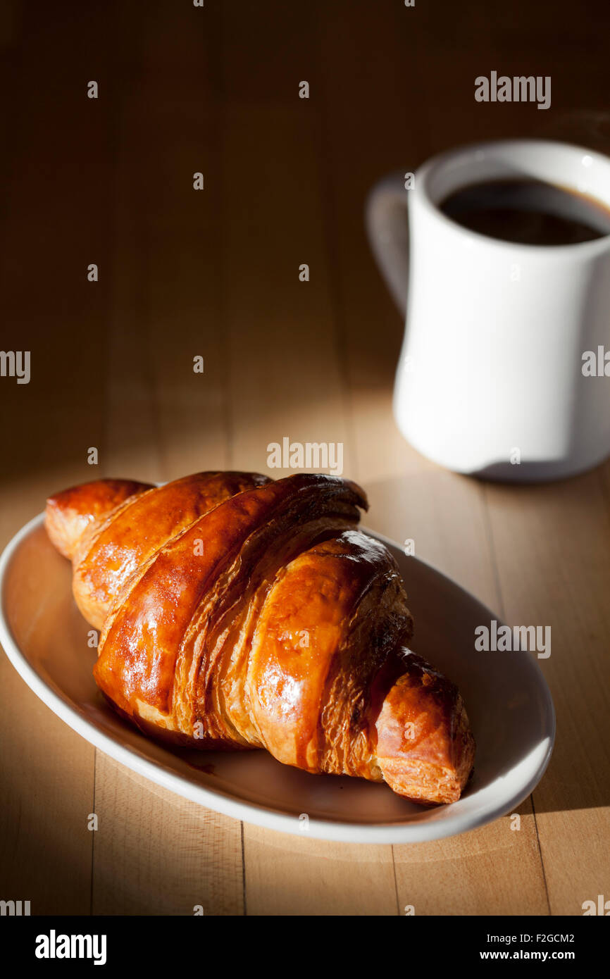 ein hell Seite beleuchtet Croissant mit einer Tasse Kaffee einen Schatten auf einen Tisch aus Stockfoto