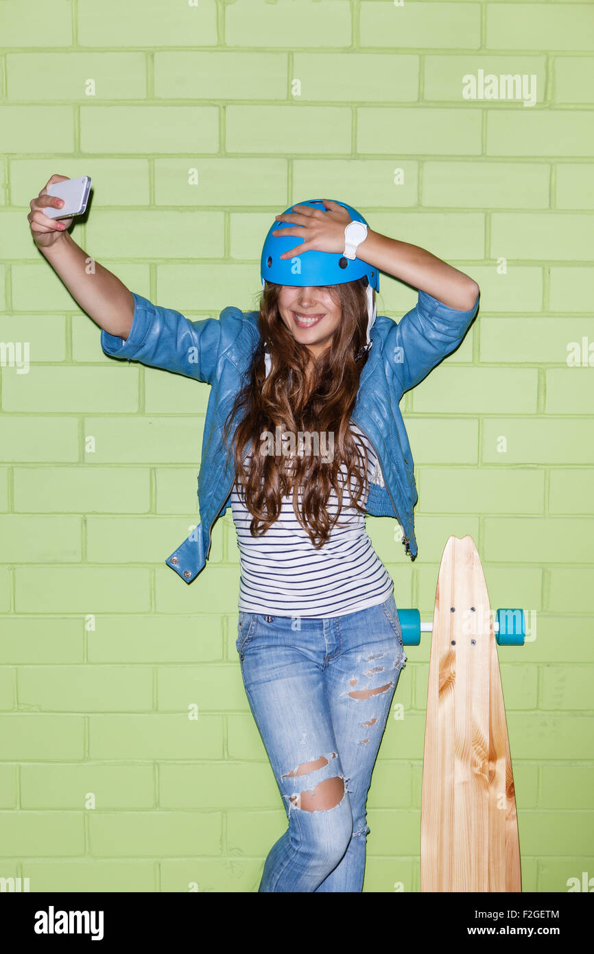 junge schöne langhaarige Brünette Mädchen im blauen Helm mit hölzernen Longboard Skateboard unter einem Selfie Selbstporträt von di Stockfoto