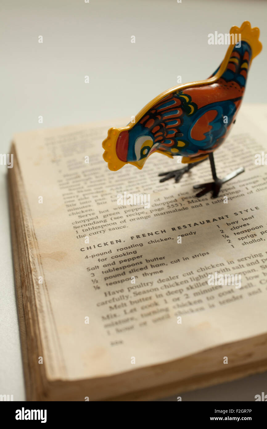 Eine antike Metall Spielzeug Huhn posiert auf einem alten Kochbuch. Stockfoto