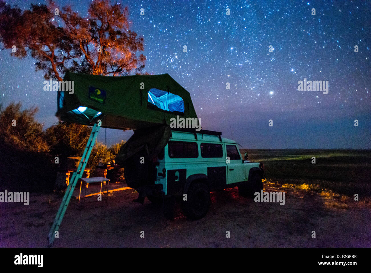 Land Rover geparkt mit einem Pop-up-Zelt auf dem Dach unter dem Nachthimmel in Botswana, Afrika Stockfoto