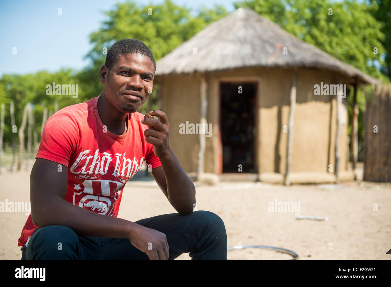 Afrikanischer Mann sitzt vor Strohdach-Hütte in Botswana, Afrika Stockfoto