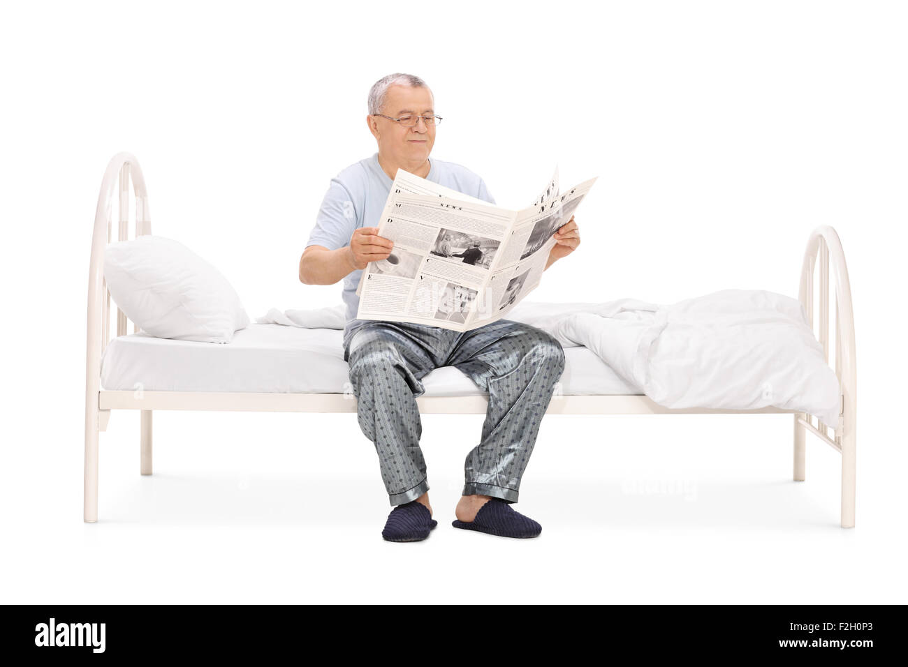 Ältere Mann im Pyjama liest eine Zeitung sitzt auf einem Bett isoliert auf weißem Hintergrund Stockfoto