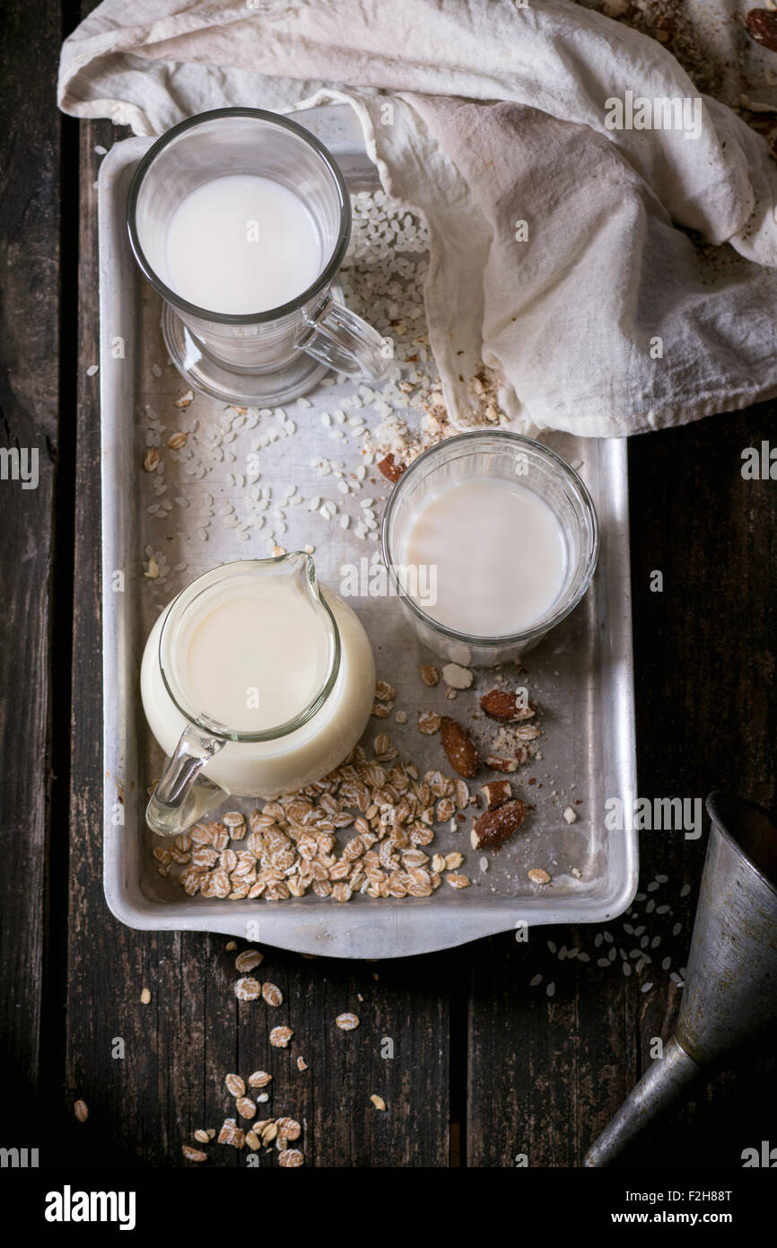 Satz von Nichtmilchprodukten Milch (Reismilch, Mandelmilch und Hafermilch) in Glasschalen und Krug auf alten Aluminium-Tablett mit Reiskörnern, Hafer fla Stockfoto
