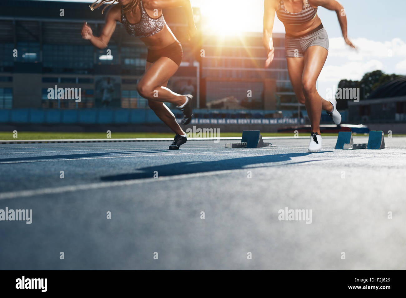 Sprinter beginnt aus den Blöcken auf Leichtathletik-Rennstrecke mit hellem Sonnenlicht. Niedrige Abschnitt Schuss der weiblichen Athleten starten eine r Stockfoto