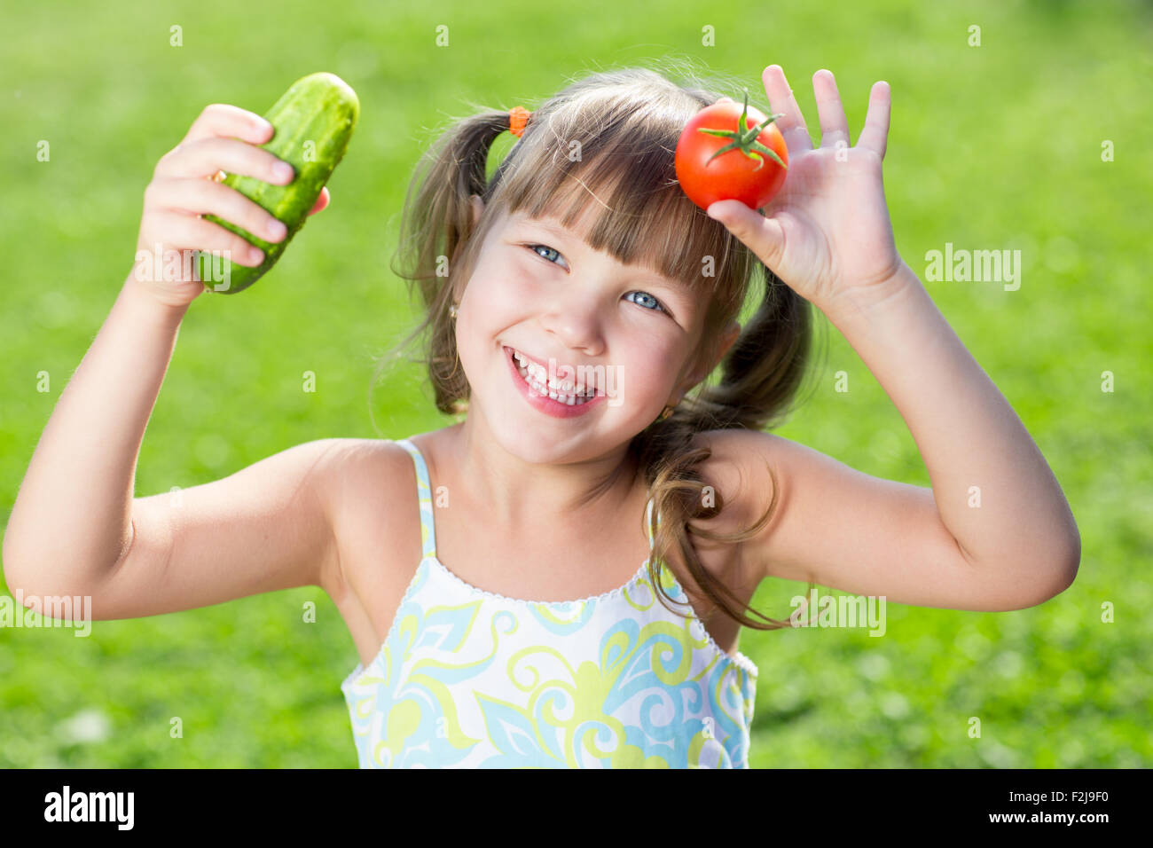 Glückliche kleine Mädchen über den Rasen mit einem Gemüse im Sommer. Konzept von gesunden Lebensmitteln. Stockfoto