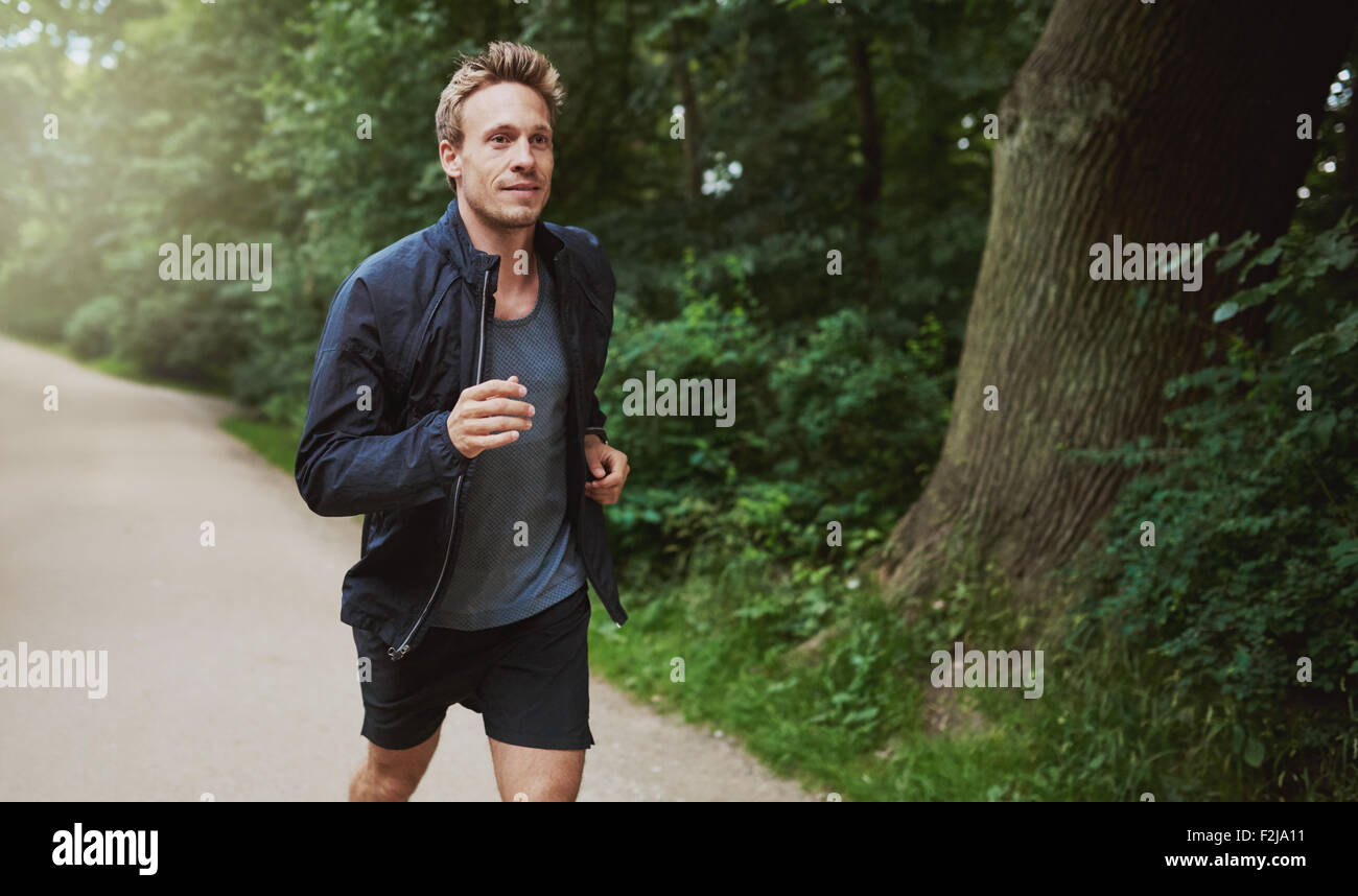 Drei Viertel Schuss eines gesunden jungen Mannes in Jacke Hemd, Joggen im Park in den frühen Morgenstunden. Stockfoto