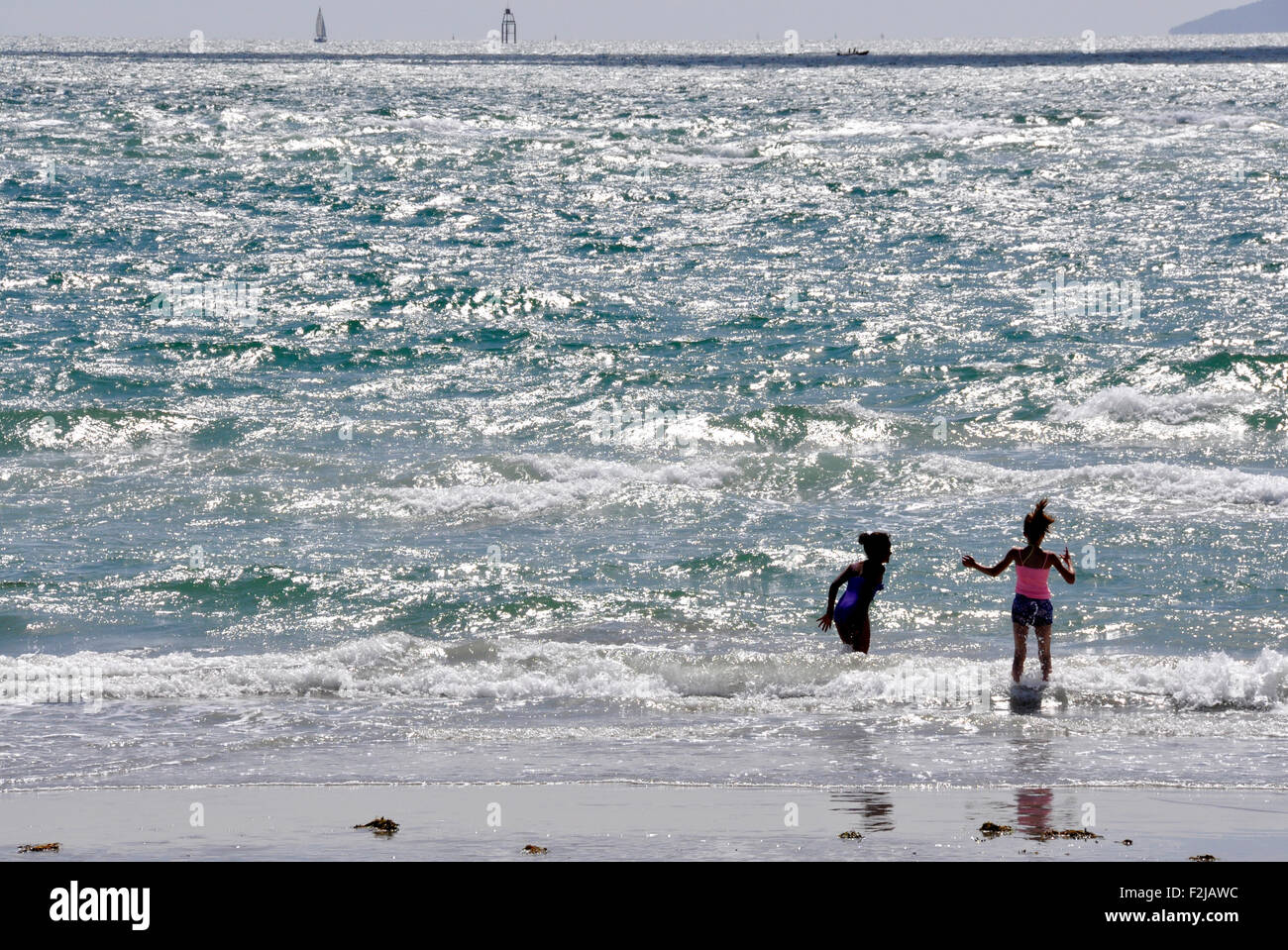 Gegen das Licht - am Meer - glitzernden Wellen - sandigen Strand - paar in die brechenden Wellen - voller Leben und Spaß zu spielen Stockfoto