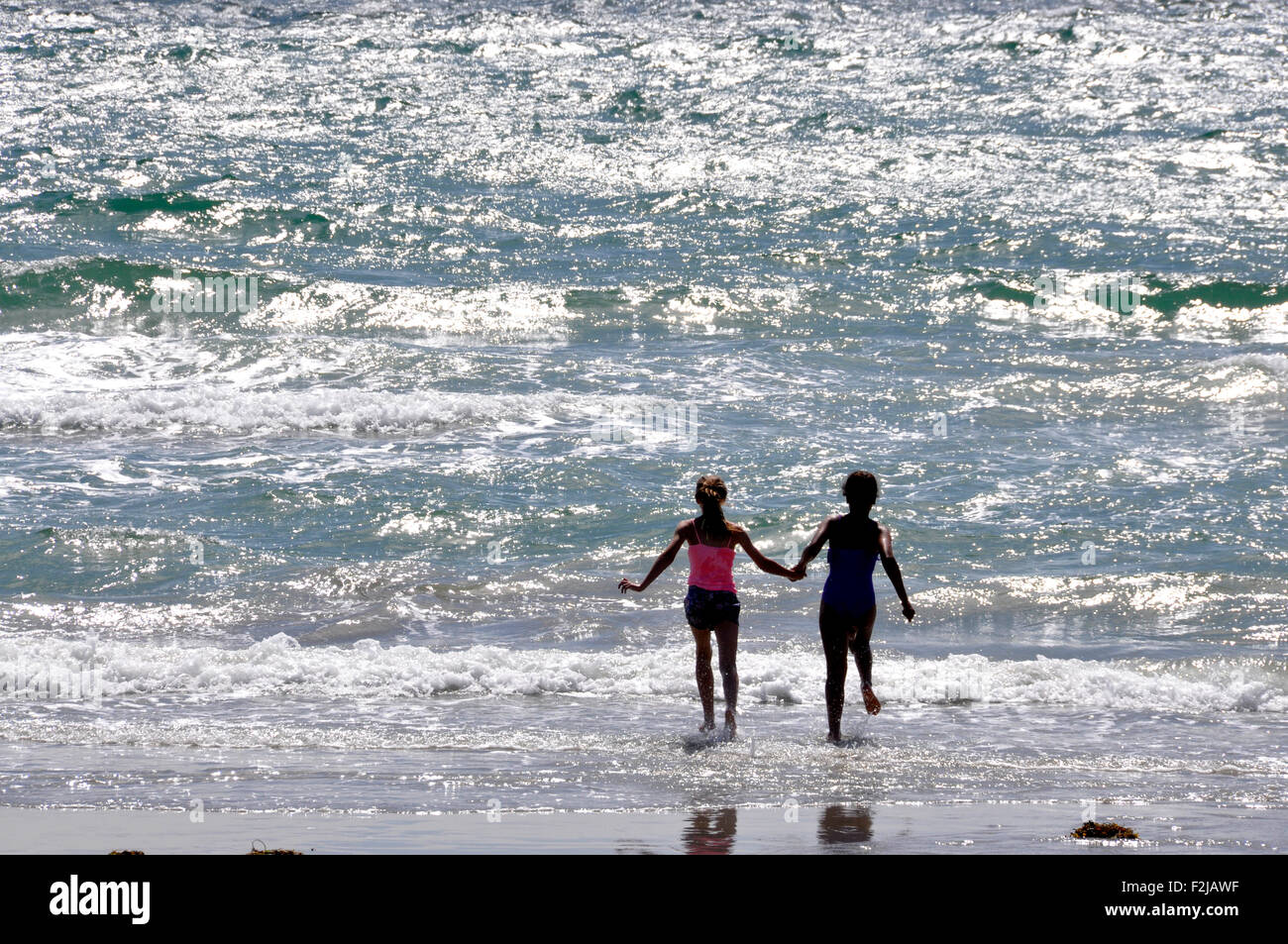 Gegen das Sonnenlicht Seascape - glitzernde Wellen brechen sich am Sandstrand - junges Paar laufen hand in hand in die Brandung Stockfoto