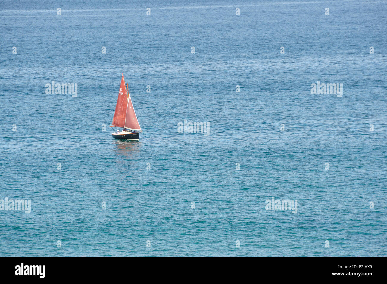 Rote Segel auf einem blauen Meer - ein Segelschiff - rote Segel - allein auf einem tiefblauen Meer - Sonne - ruhiger See Stockfoto