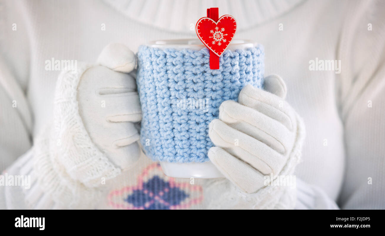 Gestrickter Wolle-Cup in Menschenhand. Mit roten Herzen. Stockfoto