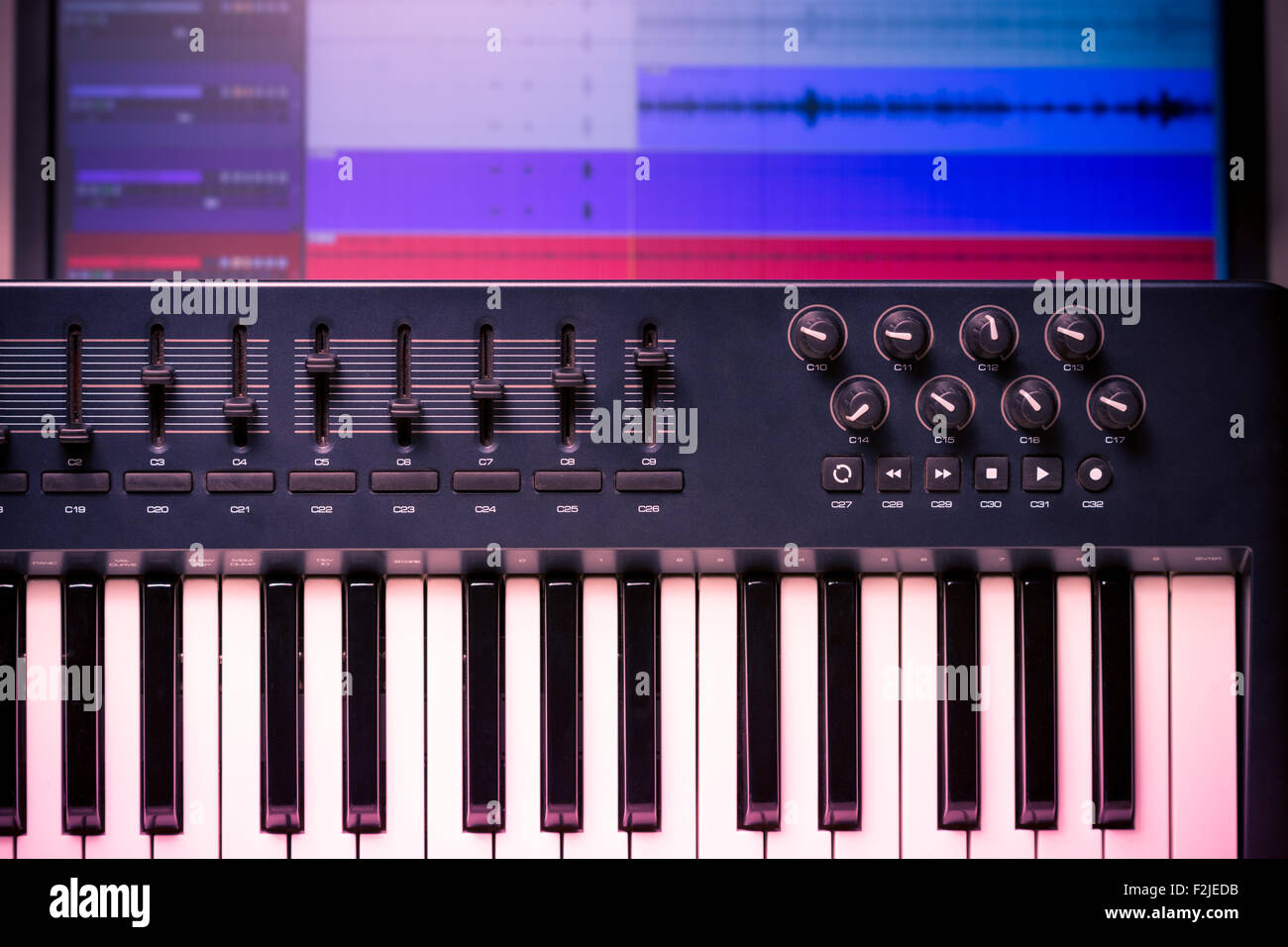 MIDI-Keyboard und Controller mit Fadern und Tasten. Wellenformen in eine DAW sind sichtbar im Hintergrund Stockfoto