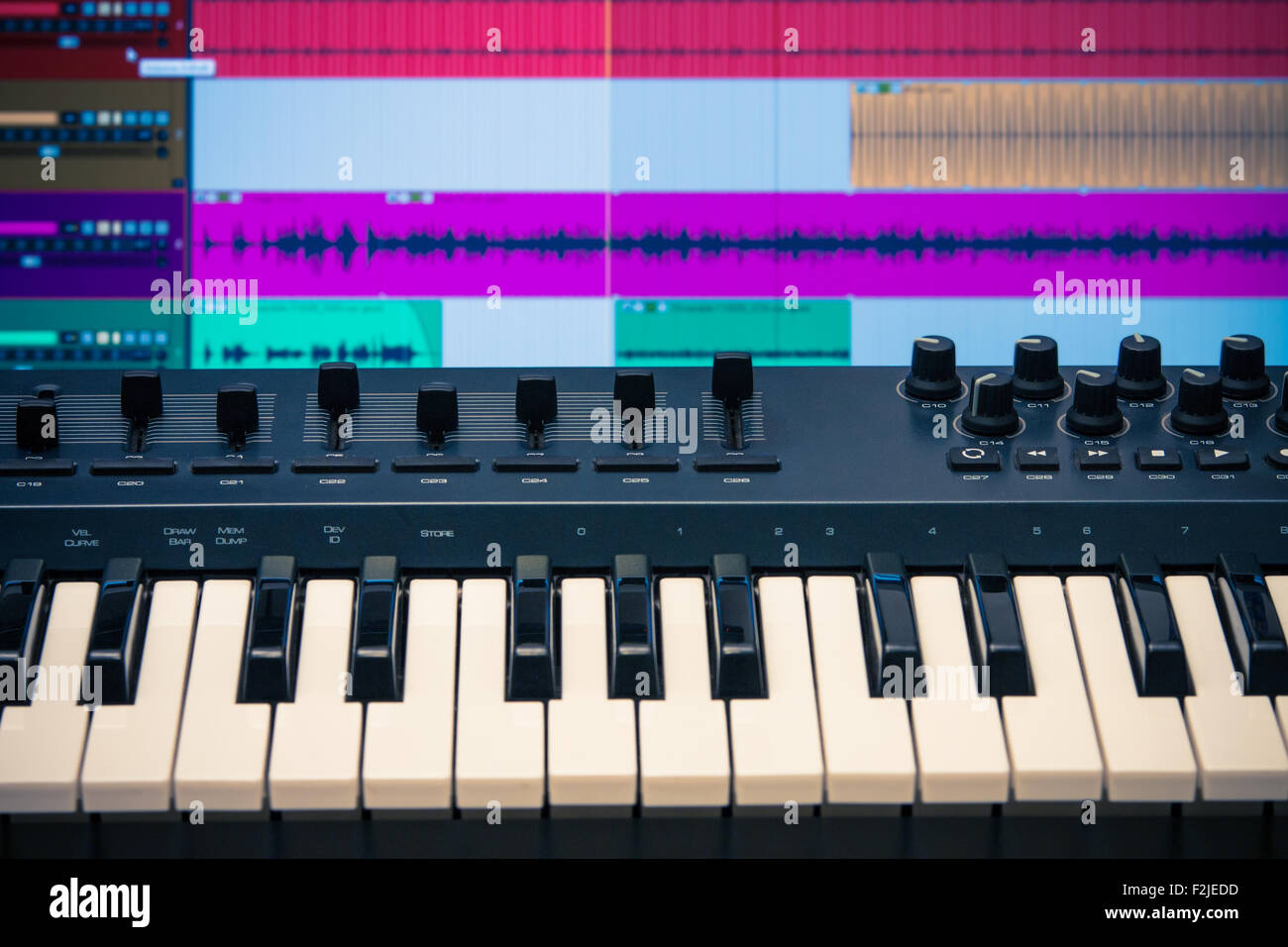 MIDI-Keyboard und Controller mit Fadern und Tasten. Wellenformen in eine DAW sind sichtbar im Hintergrund Stockfoto
