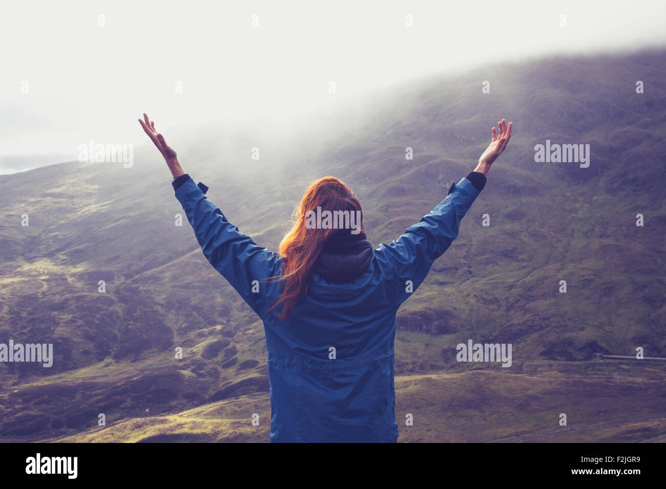 Junge Frau hob die Arme in Freude auf einem Berggipfel Stockfoto