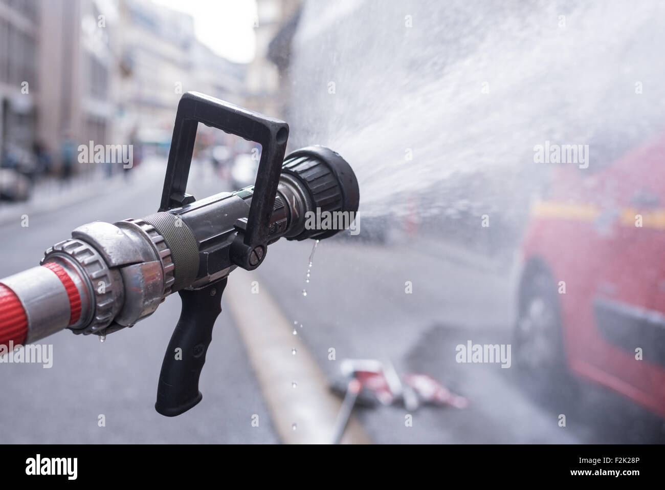 Wasserstrahl spritzt aus eine Brandbekämpfung Firehose-Düse mit einem roten Kämpfer Feuerwehrauto in Paris Stockfoto