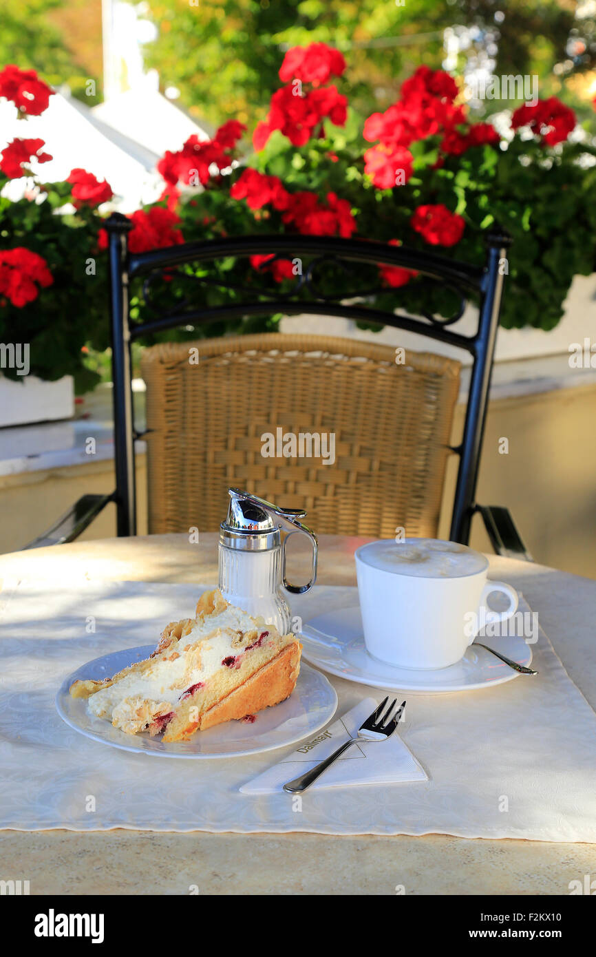 Kaffee und eine große Sahnetorte in deutscher Kaffee shop mit leuchtend roten Blüten. Stockfoto