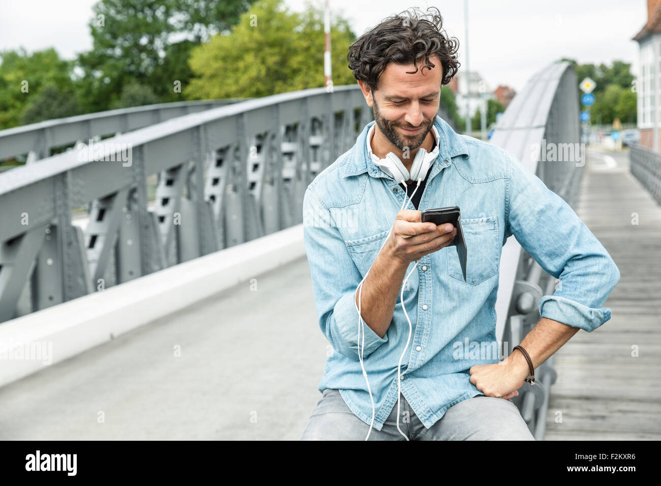 Lächelnder Mann auf einer Brücke Blick auf Handy Stockfoto