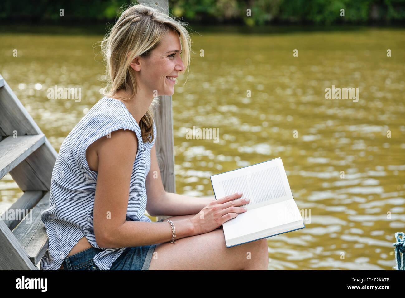 Lächelnde junge Frau Lesebuch an der waterfront Stockfoto