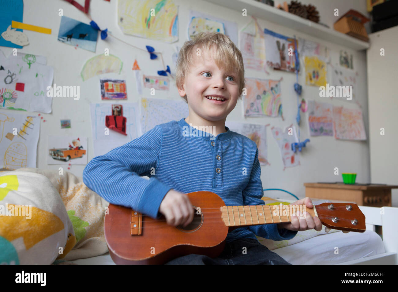 Porträt von lächelnden kleiner Junge sitzt auf seinem Bett seines Zimmers, Gitarre spielen Stockfoto