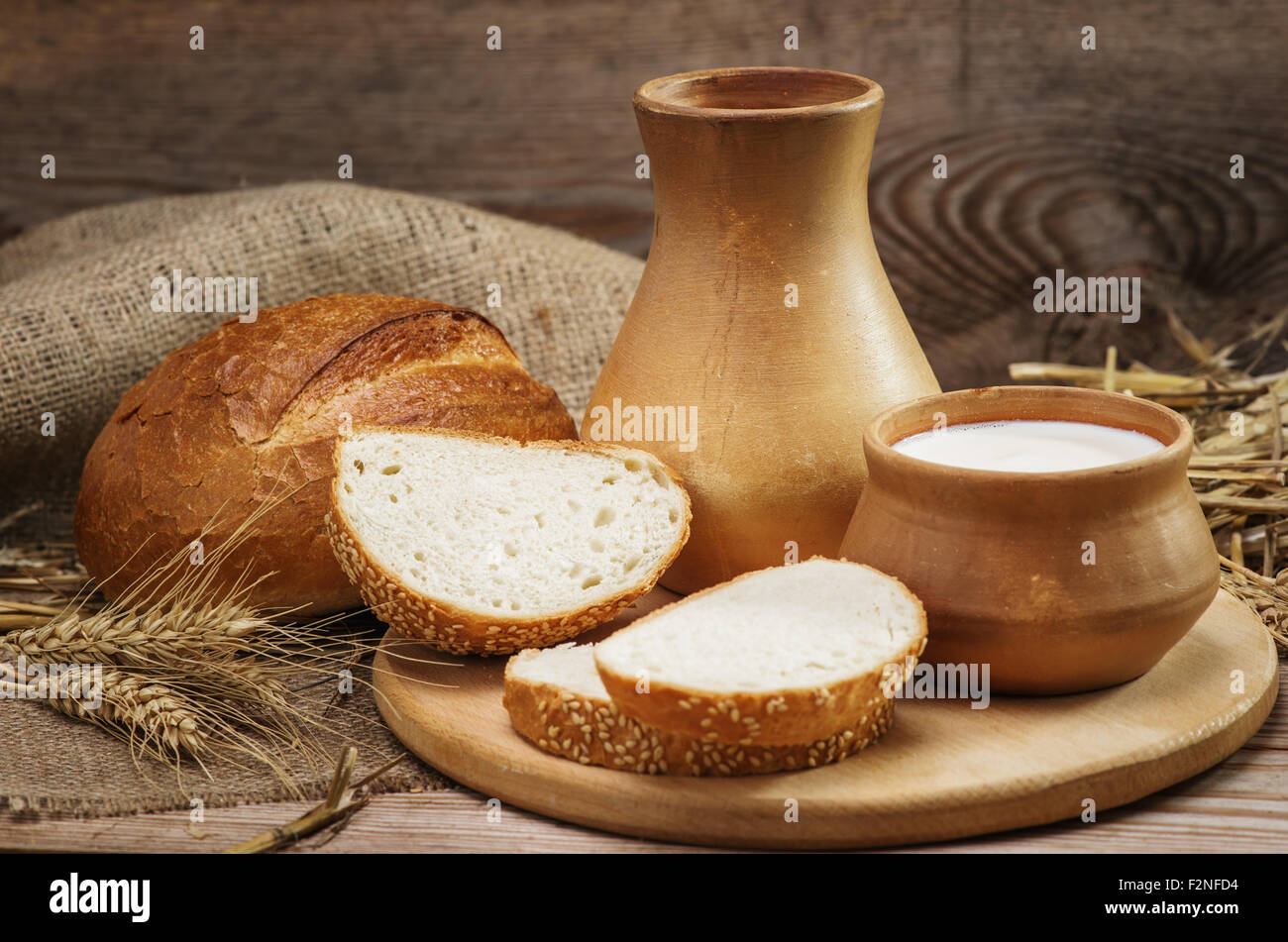 Brot und Backwaren und Milch in einem Tonkrug und Schüssel, Halme des Weizens, Sackleinen auf den alten hölzernen Hintergrund Stockfoto