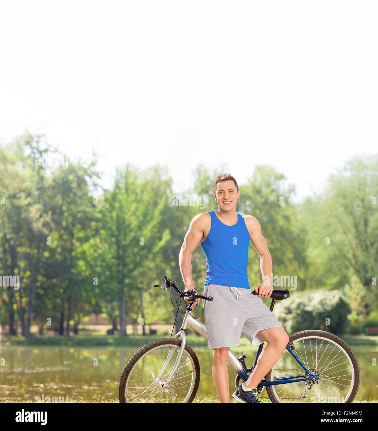 Fröhliche junge Radfahrer mit seinem Fahrrad von einem Teich in einem Park posiert mit Tilt-Shift-Objektiv geschossen Stockfoto