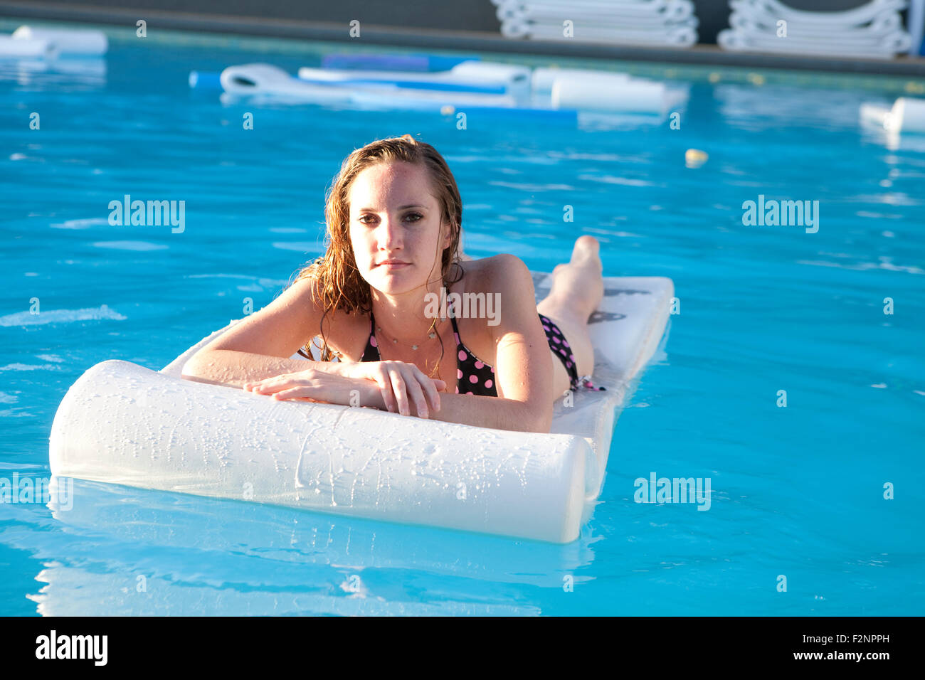 Frau schwimmt auf Floß im Schwimmbad Stockfoto