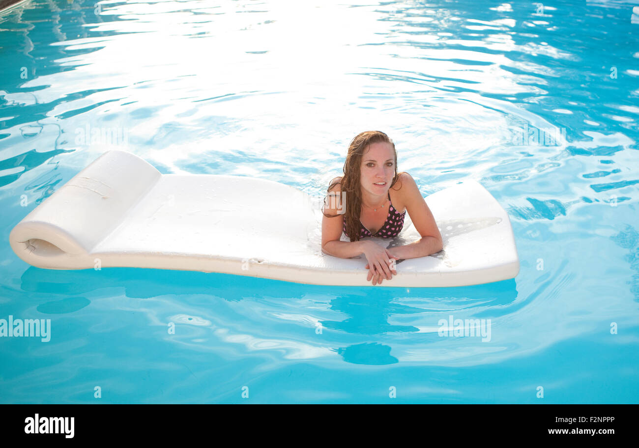Frau schwimmt auf Floß im Schwimmbad Stockfoto