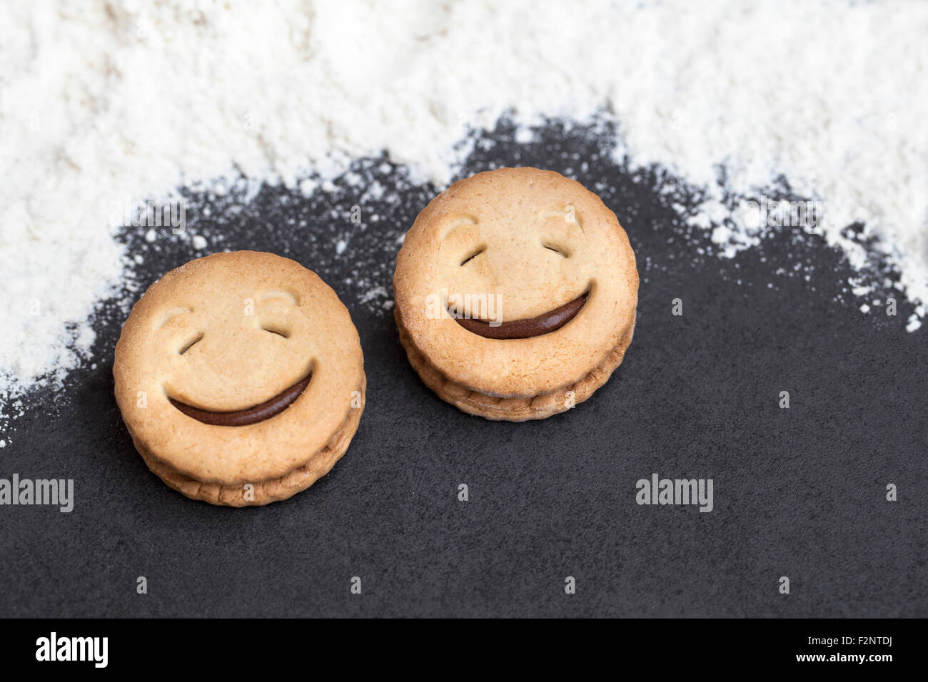 Zwei lachende Gesichter der Cookie in einer dunklen Background mit Mehl um. Stockfoto