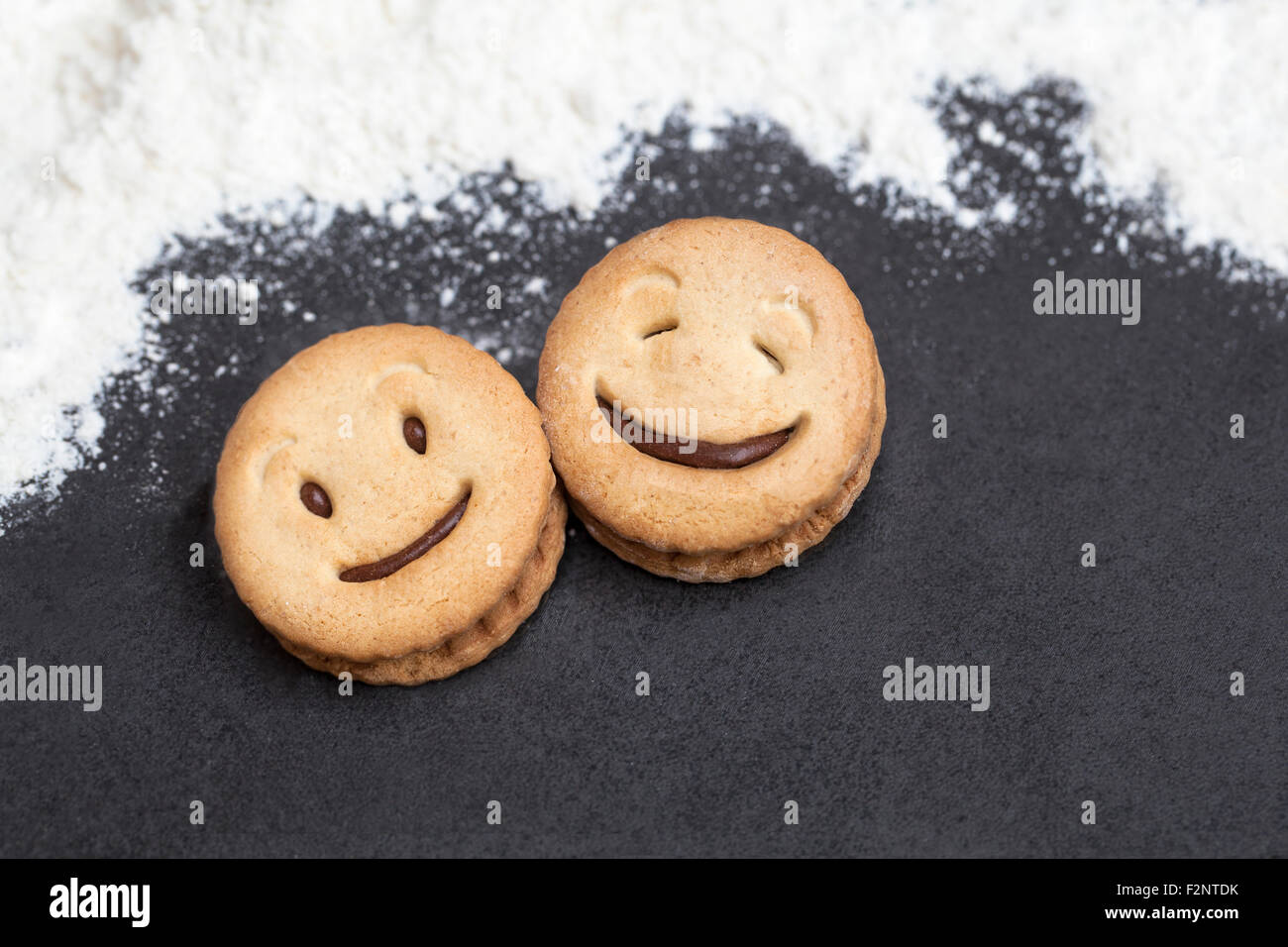 Zwei lachende Gesichter der Cookie in einer dunklen Background mit Mehl um. Stockfoto