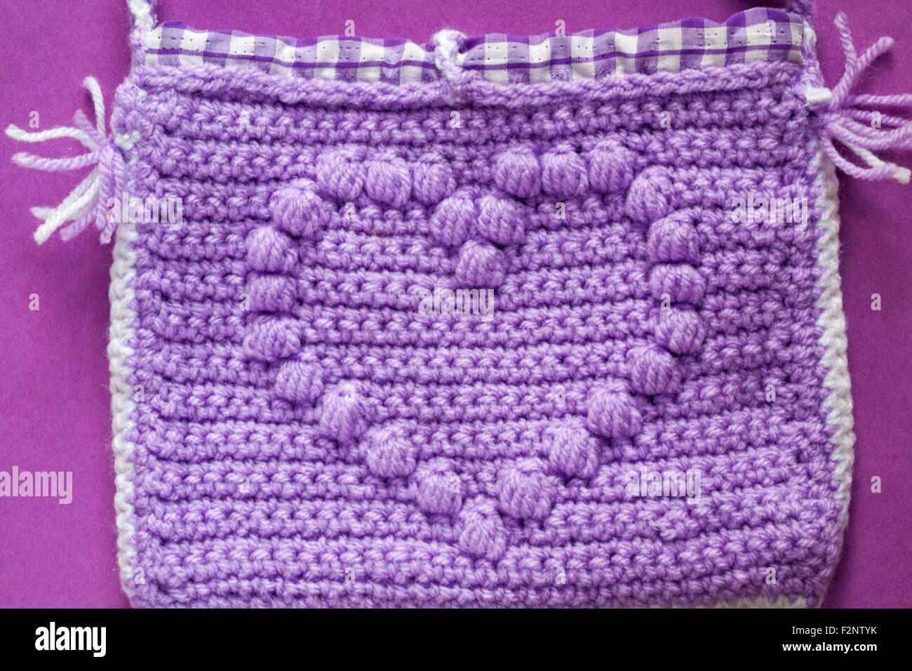 Mauve dekorative gestrickte Tasche mit Herz auf lila Hintergrund Stockfoto