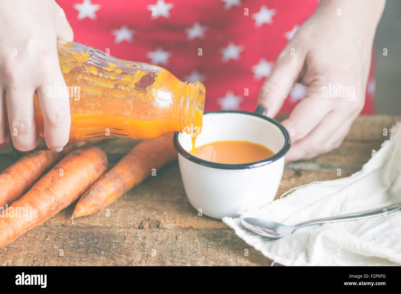 Die Frau gießt eine Flasche Karottensaft in eine Tasse Stockfoto
