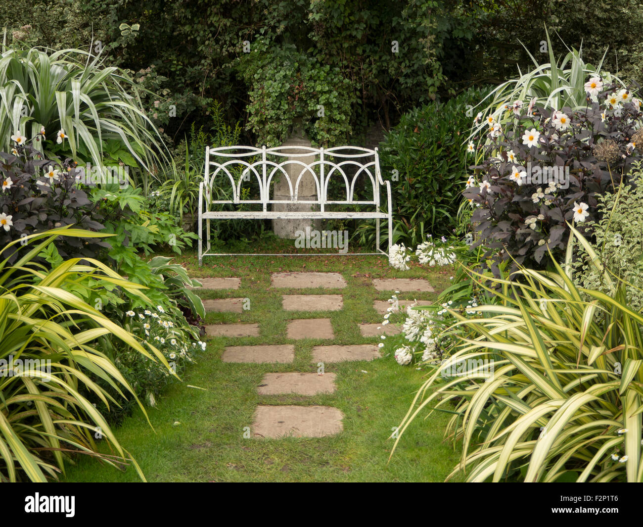 Der weiße Garten, Chenies Manor im Spätsommer zeigt weiße Dahlien, bunte Blätter, Pflastersteine und weiße Sitzbank. Stockfoto