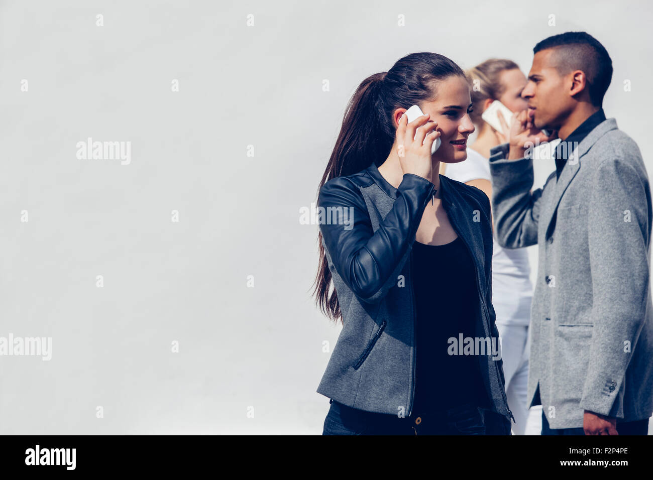 Junge Frau mit Smartphone vor zwei anderen Menschen telefonieren Stockfoto
